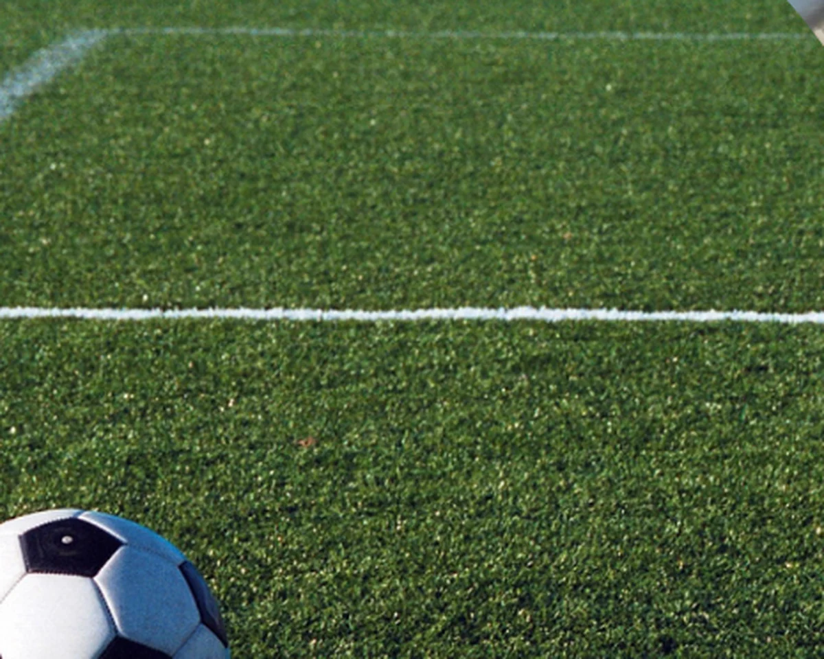 Gramado de campo esportivo com linha demarcatória e bola de futebol sobre a grama